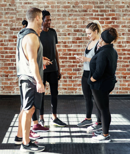 Toma dos. un alegre grupo de jóvenes de pie en un círculo y tener una conversación antes de un entrenamiento en un gimnasio - Foto, Imagen