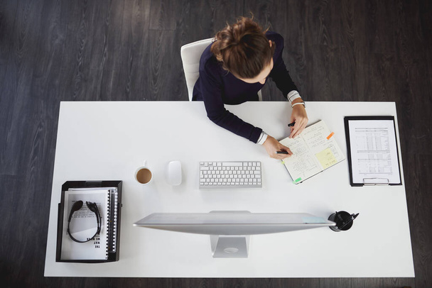 Lo tengo todo planeado. Foto aérea de una joven empresaria irreconocible sentada en su escritorio y escribiendo notas en una oficina moderna - Foto, imagen