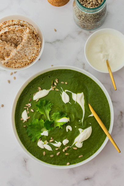 Healthy breakfasts, green broccoli and spinach cream soup with sunflower seeds and yogurt, buckwheat bread, top view - Photo, Image