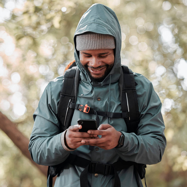 Hombre negro, teléfono y sonrisa para la comunicación senderismo, redes sociales o chat en la naturaleza al aire libre. Hombre africano feliz o excursionista sonriendo en el teléfono inteligente móvil para trekking, viajes o ubicación en línea. - Foto, Imagen