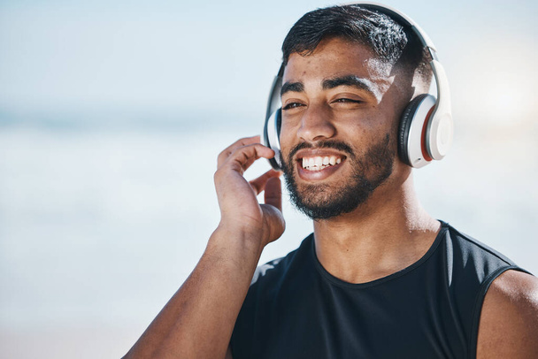Happy, beach and a man with music for fitness, running motivation and ideas in nature. Smile, wellness and an athlete listening or streaming a podcast while training or exercise vision at the sea. - Fotografie, Obrázek