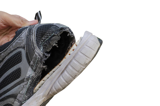 Рука держа старый, разорванный черный ботинок за пяткой обуви изолированы на белом фоне с обрезкой пути - Фото, изображение