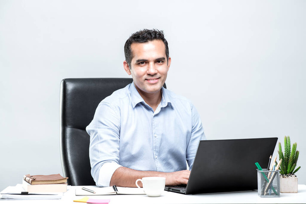 Aasialainen miespuolinen toimistotyöntekijä istuu kannettavan tietokoneen ääressä pöydän ääressä ja hymyilee toimistossa - Valokuva, kuva