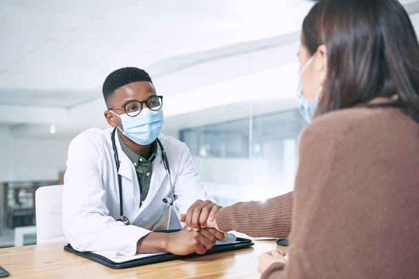 This isnt something you cant handle. a young doctor sitting with his patient and wearing a face mask while comforting her in the clinic - Foto, Bild