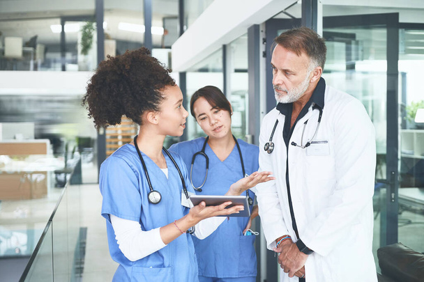 Мне нужно было мнение эксперта. красивый зрелый врач, стоящий со своими медсестрами и использующий цифровые таблетки во время обсуждения - Фото, изображение