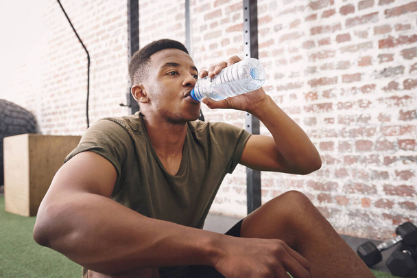 The one thing we cant live without is water. a sporty young man drinking a bottle of water at the gym - Foto, imagen