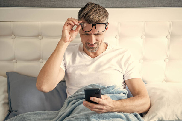 mature man in bed chatting on phone wearing eyeglasses. eyecare. - Fotó, kép