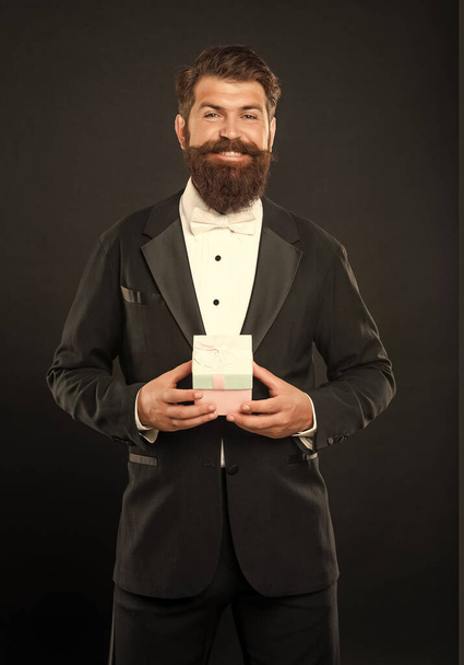 cheerful man in tuxedo bow tie formalwear on black background with business reward box. occasion greeting. - 写真・画像