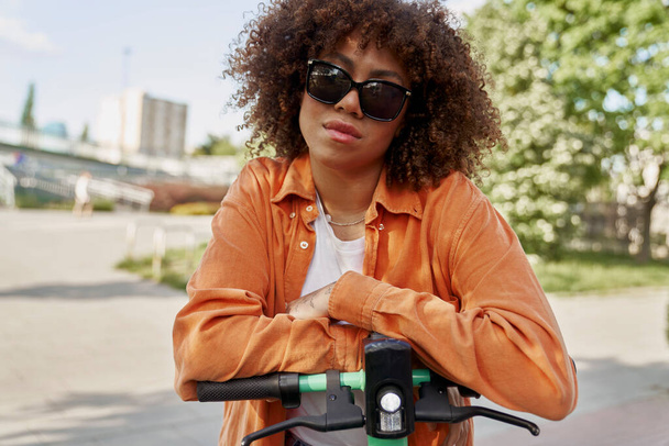 Frontansicht einer schwarzen Frau mit Sonnenbrille auf einem Elektroroller  - Foto, Bild