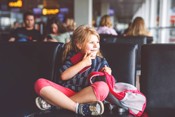 Little girl at the airport waiting for boarding at the big window. Cute kid holding passport..Looking forward to leaving for a family summer vacation. - Foto, immagini
