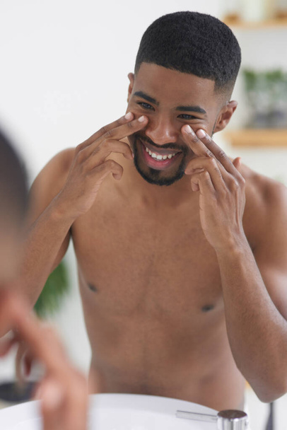 Happy man, face and beauty with mirror and facial, hygiene and grooming during morning routine at home. Male person with smile in bathroom, fresh and clean skincare with wellness and moisturizing. - Photo, Image
