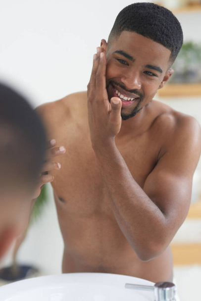 Boldog ember, arc és szépség tükörrel és bőrrel, higiénia és ápolás reggeli rutin otthon. Fekete férfi személy mosoly a fürdőszobában, friss és tiszta arc wellness és hidratáló. - Fotó, kép