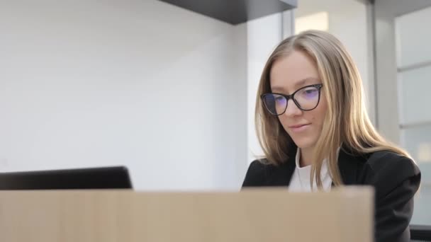 Jeune femme en lunettes travaille à l'ordinateur dans le bureau. Un sourire agréable d'un employé heureux. - Séquence, vidéo