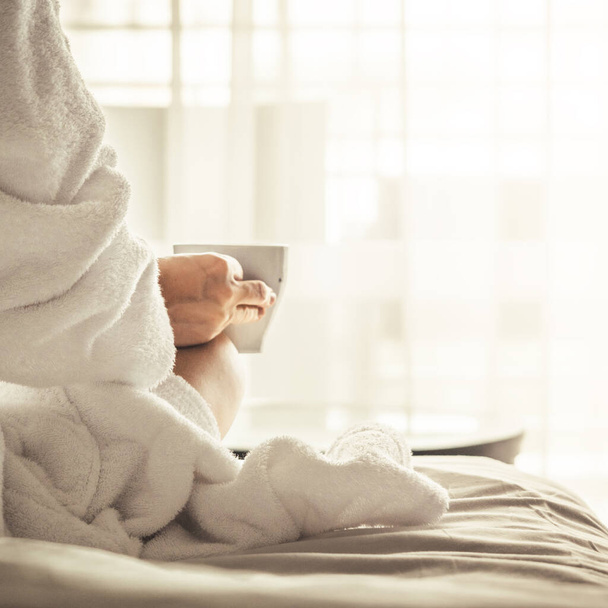 Woman in white bathrobe and towel lying on sofa and relaxing with tea at the roof of hotel - Foto, Imagem