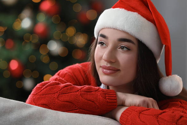 Beautiful woman wearing red Christmas hat against blurred lights - Valokuva, kuva
