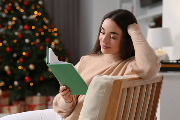 Woman reading book near Christmas tree indoors - Foto, Imagen