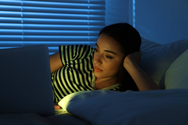 Young woman using laptop on bed at night. Internet addiction - Φωτογραφία, εικόνα