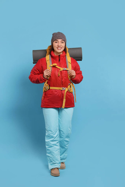 Smiling young woman with backpack walking on light blue background. Active tourism - Фото, зображення