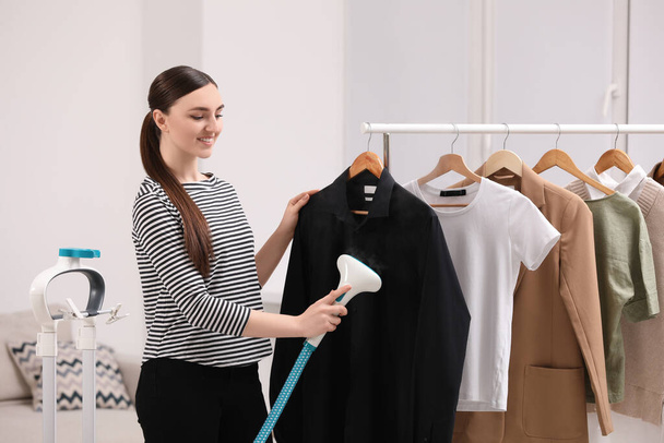 Woman steaming black shirt on hanger at home - Zdjęcie, obraz