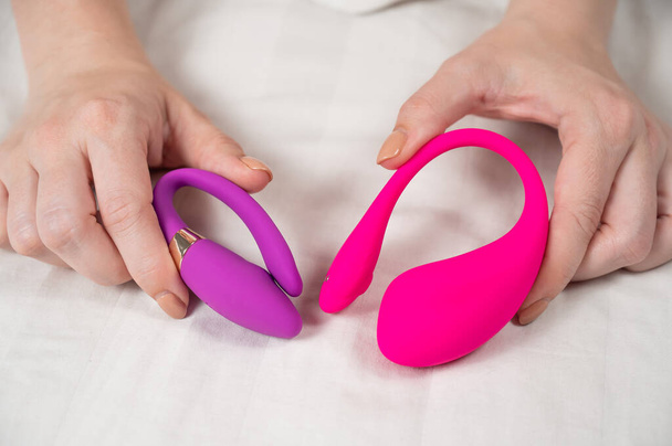 Woman holding pink and purple vibrators while lying in bed - Foto, immagini