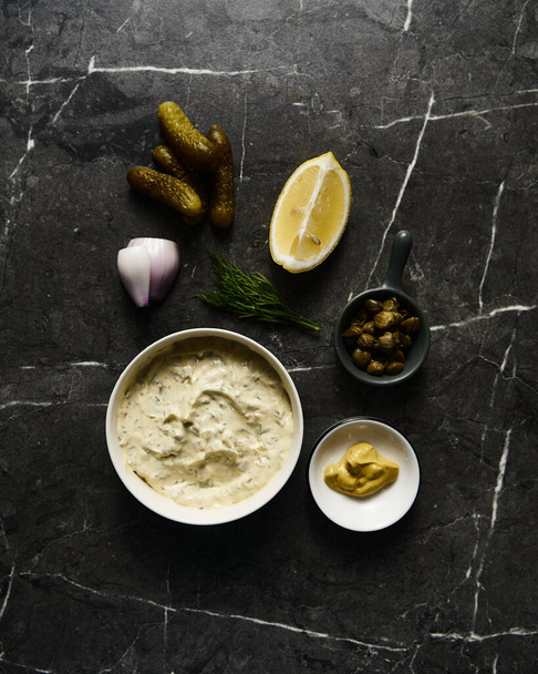 Classic Tartar Sauce with it ingredients on dark stone or marble background. Mayonnaise with dill and pickled cucumbers with lemon. Top view food photo. FlatlayHigh quality photo - Foto, Imagem