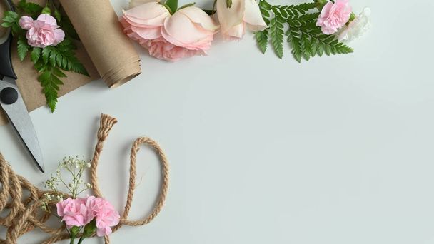 Floristischer Arbeitsplatz. Rosa Blüten, Scheren, Packpapier und Blätter auf weißem Hintergrund mit Kopierraum. - Foto, Bild