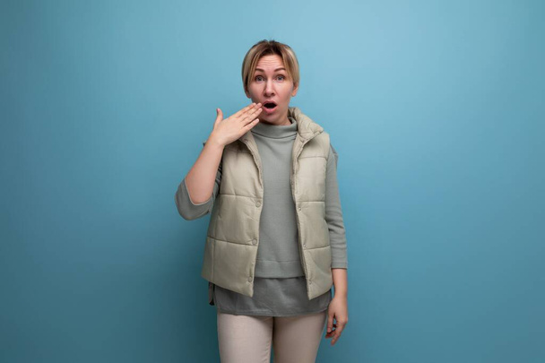 sorprendida mujer rubia de 30 años en chaleco casual sobre fondo azul estudio. - Foto, imagen