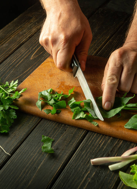 Cocinar una ensalada dietética para el almuerzo a partir de verduras frescas y hojas de acedera. Las manos del chef cortan acedera en una tabla de la cocina con un cuchillo. Alimentación vegetal fresca útil. - Foto, Imagen