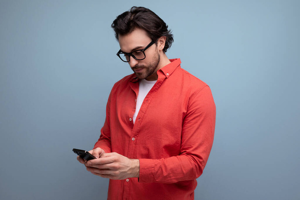 smart young brunette man in glasses and red shirt chatting on the phone. - Photo, Image