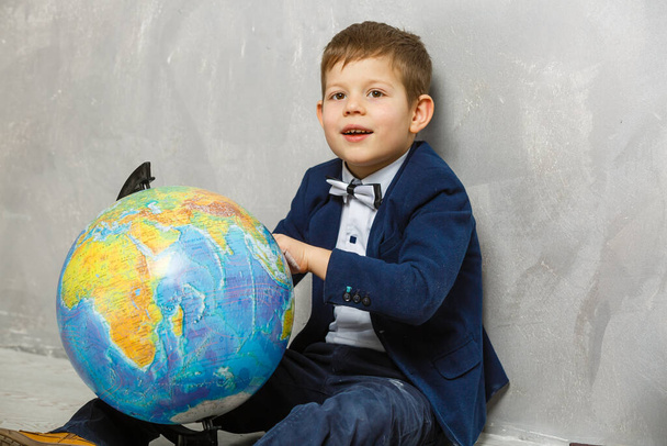 Söpö valkoihoinen koulupoika istuu luokkahuoneessa ala-asteella. Pieni poika Globen vieressä. Takaisin kouluun käsite. - Valokuva, kuva