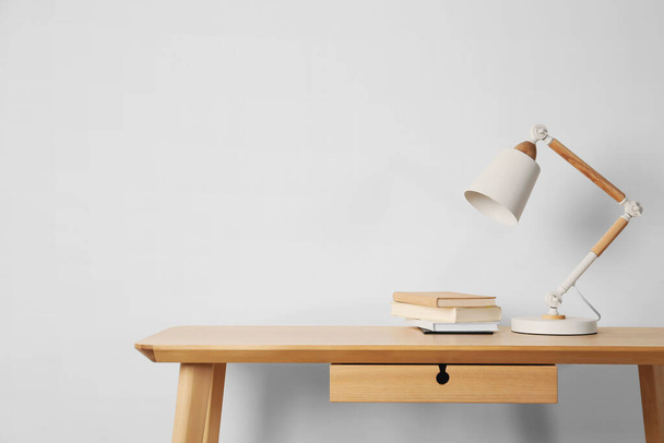 Stilvolle moderne Schreibtischlampe und Bücher auf Holztisch neben weißer Wand - Foto, Bild