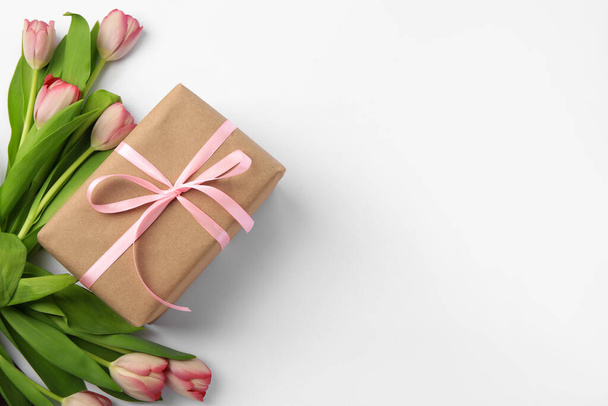 Beautiful gift box with bow and pink tulips on white background, flat lay. Space for text - Foto, imagen