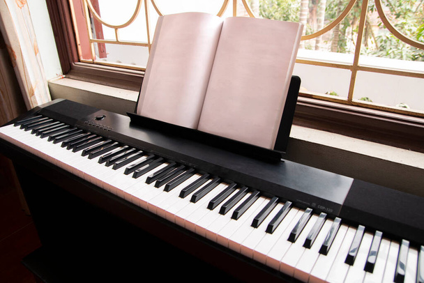 Piano eléctrico con partitura vacía cerca de la ventana vista lateral derecha - Foto, Imagen