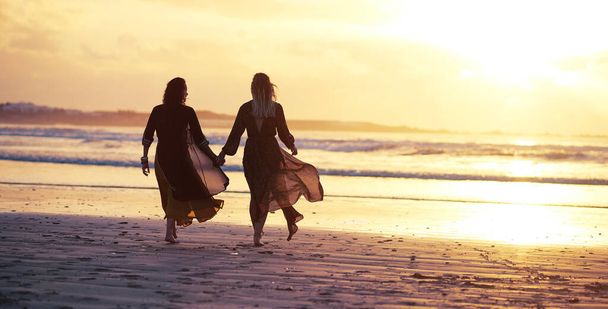 Tus alas ya existen, así que sigue adelante y vuela. dos mujeres jóvenes pasando el día en la playa al atardecer - Foto, imagen
