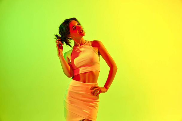 Image with charming girl, young woman smiling with dreaming face over acid green color studio background in neon light. Concept of beauty, youth, human emotions, fashion, cosmetology, ad - 写真・画像