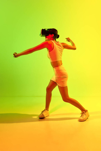 Walka o rzeczywistość wirtualną. Dziewczyna w okularach VR gra na kwaśne zielone i żółte tło. Młodzież, wirtualny styl życia przyszłości. Koncepcja nierealnego świata, digitalizacja, technologia, reklama - Zdjęcie, obraz