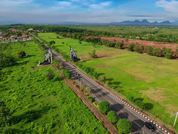 Ilmakuva rajaportille Purwakartassa. Drone näkymä asfalttitiet perinteinen portti ja vihreä istutukset.  - Valokuva, kuva