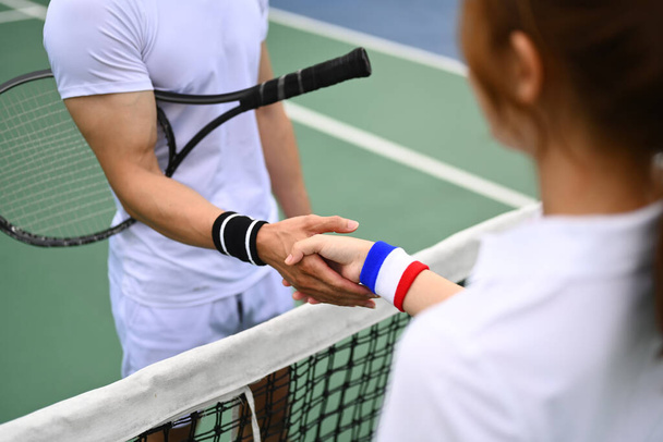 Gehakt schot van mannelijke en vrouwelijke tennissers schudden handen over het net tijdens de wedstrijd aan het hof. - Foto, afbeelding