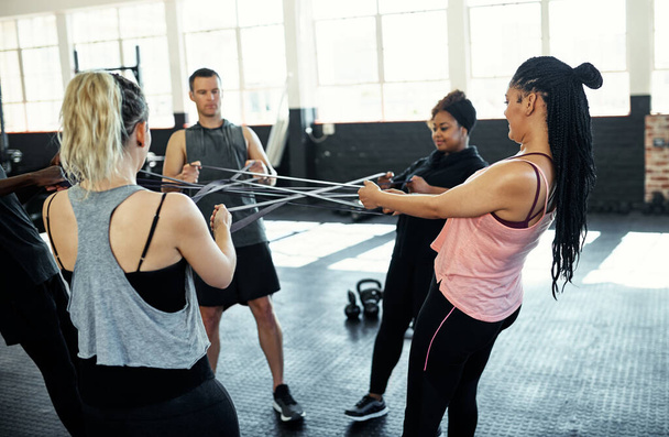 Podéis lograr mucho más juntos. un grupo de fitness haciendo ejercicio con bandas de resistencia en su sesión en el gimnasio - Foto, Imagen