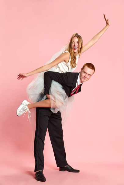 Portrait of young, beautiful, happy couple, man and woman after marriage posing against pink studio background. Woman sitting on mans back. Concept of family, relationship, youth, emotions, fun. Ad - Photo, Image