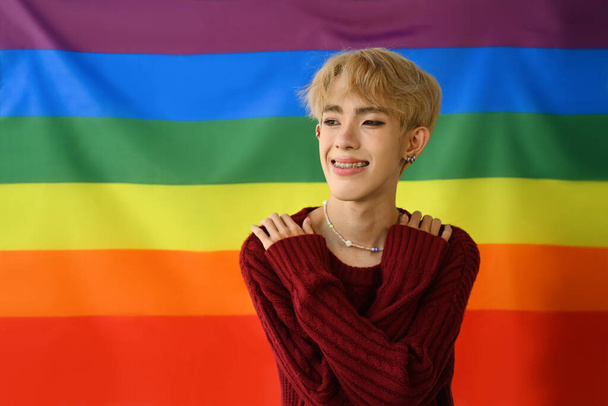 Портрет веселого гомосексуального молодого гея, позирующего на фоне радужного флага гордости. ЛГБТК, права человека и равенство социальных. - Фото, изображение