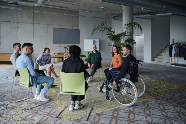 In a modern office, a diverse group of business individuals is seen gathered in a circle, engaged in lively discussions and sharing ideas about various business concepts - 写真・画像