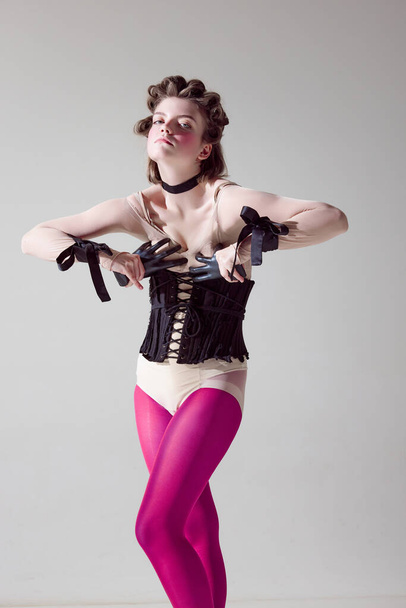 Hohe Mode. Porträt eines jungen extravaganten Mädchens in schwarzem Korsett und pinkfarbenen Strumpfhosen vor grauem Studiohintergrund. Konzept weiblicher Schönheit, Kunst, Weiblichkeit, Mode, Emotionen - Foto, Bild