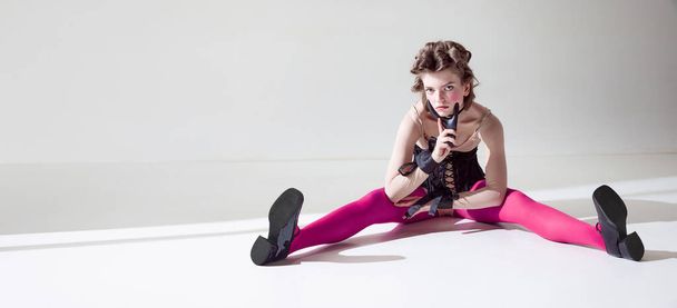 Porträt eines hübschen, außergewöhnlichen jungen Mädchens, das in schwarzem Korsett und pinkfarbenen Strumpfhosen vor grauem Studiohintergrund posiert. Konzept weiblicher Schönheit, Kunst, Weiblichkeit, Mode, Emotionen - Foto, Bild