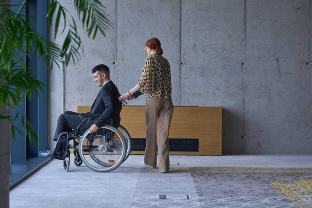 A businessman in a wheelchair and his female colleague together in a modern office, representing the power of teamwork, inclusion and support, fostering a dynamic and inclusive work environment - Φωτογραφία, εικόνα