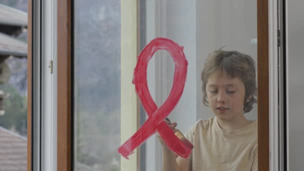 Menino de 10 anos está pintando fita vermelha no vidro da janela. Imagens 4k de alta qualidade - Filmagem, Vídeo