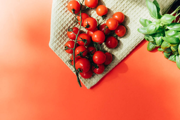 Gezonde voedselachtergrond. Een verse groente, tomaten op een groene keukendoek en groene basiliek op rode achtergrond. Vlakke plaat - Foto, afbeelding