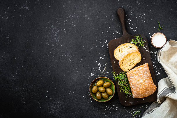 Pane di ciabatta con olive ed erbe aromatiche su nero. Cibo mediterraneo. Vista dall'alto con spazio di copia. - Foto, immagini