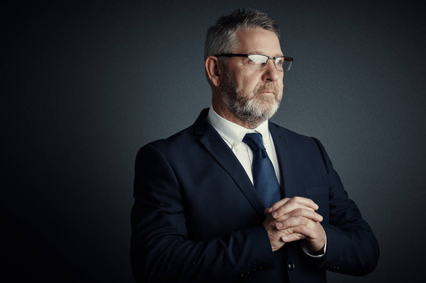 Facing business challenges with confidence. Studio shot of a handsome mature businessman looking thoughtful while standing against a dark background - Φωτογραφία, εικόνα