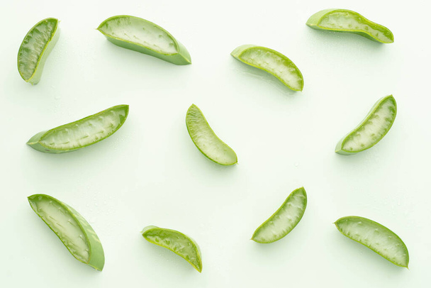 Κάτοψη της φρέσκιας φέτας φύλλων αλόης βέρα με σταγόνες νερού πάνω από πράσινο φόντο. Γέλη από τα φύλλα των φυτών αλόης που χρησιμοποιούνται για την ιατρική και την περιποίηση του δέρματος. - Φωτογραφία, εικόνα
